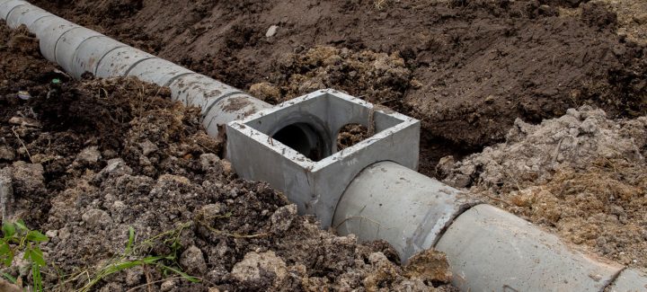 A large concrete pipe section lying on its side in a field of dirt for a drainage solution