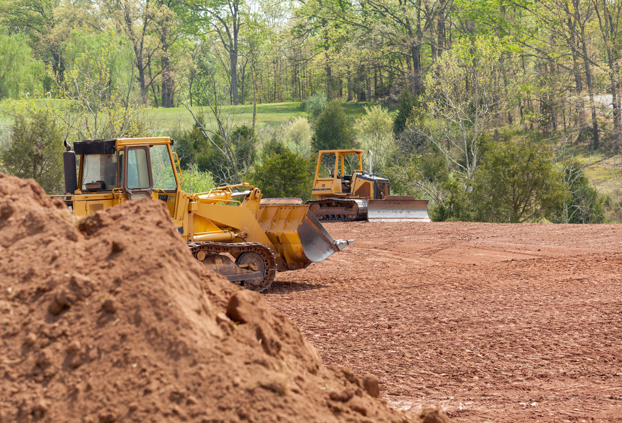 An ongoing grading work; a bulldozer moving a mass of soil in the backyard of a house.