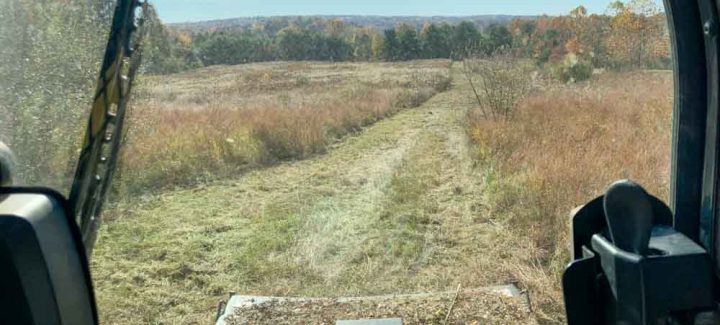 A view of a grassy field seen through an excavator equipment. The sky is clear blue.