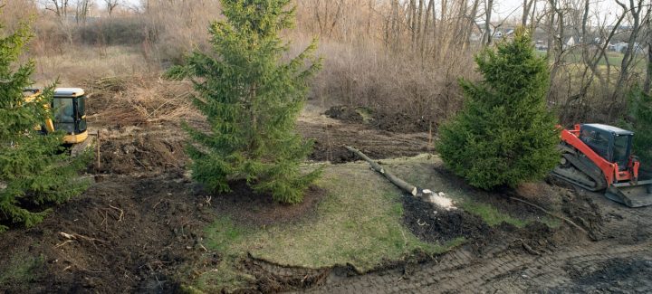 In an ongoing land clearing work: two tractors parked in a field under a clear blue sky. The closer tractor is red and the one behind it is yellow.